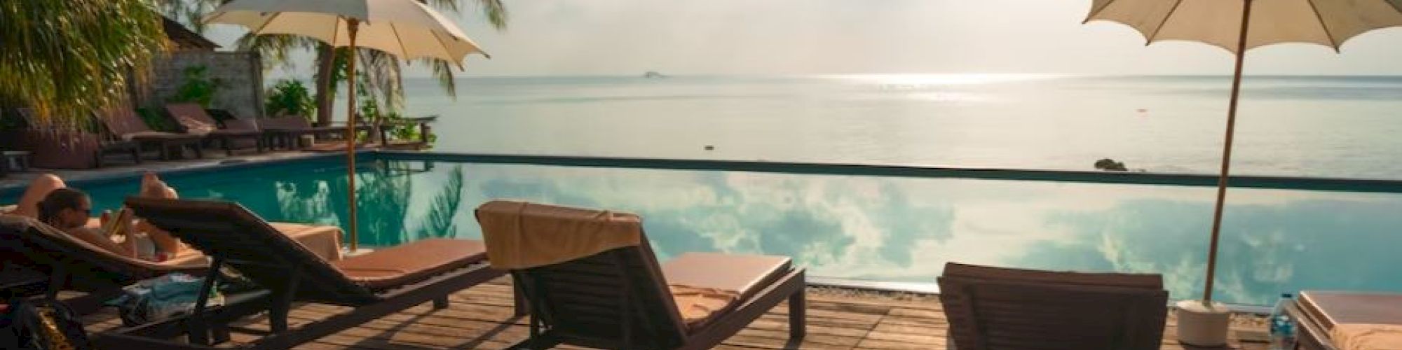 A serene poolside with lounge chairs, umbrellas, and a view of the ocean under a partly cloudy sky.