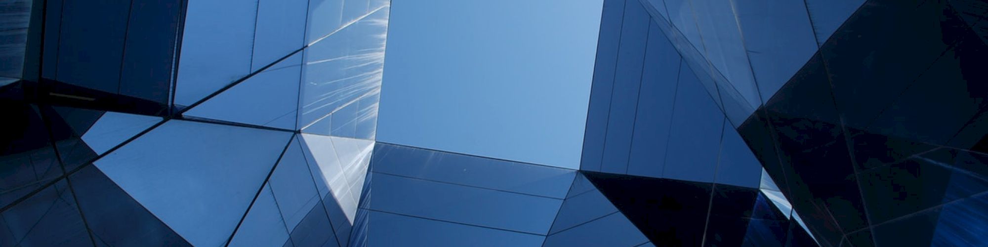 The image shows a geometric pattern of reflective glass buildings with a clear blue sky visible in the center.