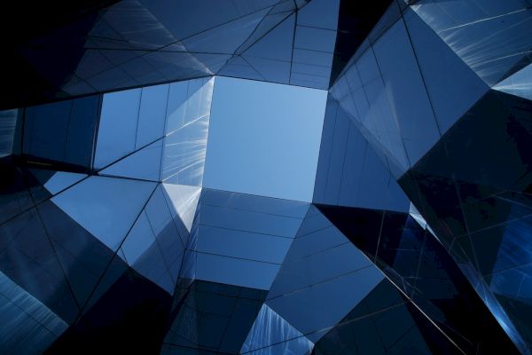 The image shows a geometric architectural design with reflective glass surfaces forming a skyward view, highlighting an opening to the sky.