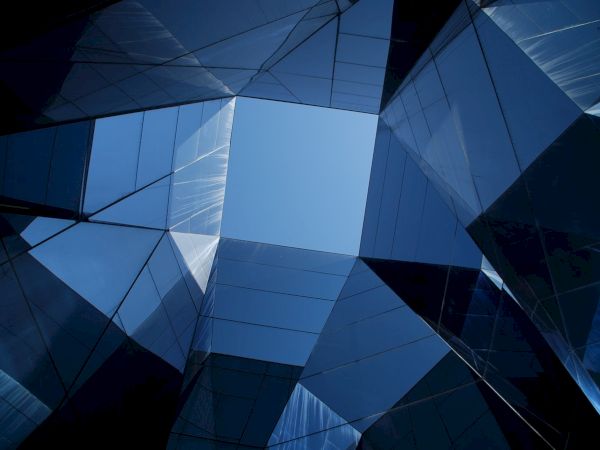 The image shows a geometric architectural design with reflective glass surfaces forming a skyward view, highlighting an opening to the sky.