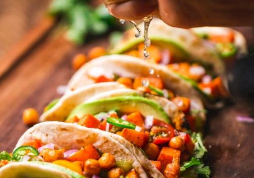 A hand squeezes lime juice over tacos filled with chickpeas, diced veggies, and avocado slices on a wooden board.
