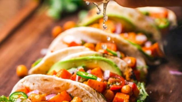 A hand squeezes lime juice over tacos filled with chickpeas, diced veggies, and avocado slices on a wooden board.
