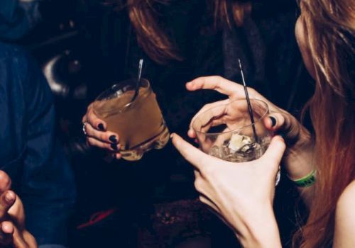 People are enjoying a night out, holding drinks with straws and smiling. The atmosphere appears lively and social.