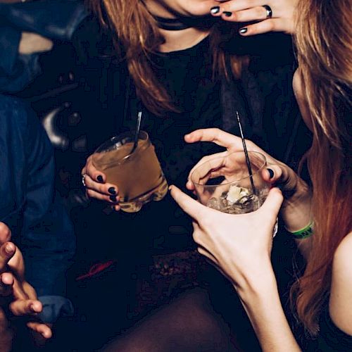 People are enjoying a night out, holding drinks with straws and smiling. The atmosphere appears lively and social.
