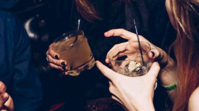 People are enjoying a night out, holding drinks with straws and smiling. The atmosphere appears lively and social.