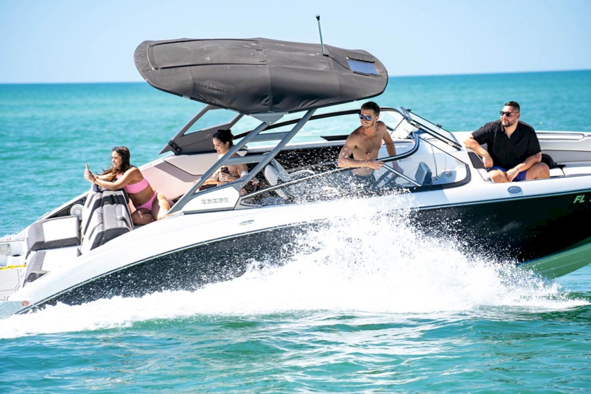A group of people is enjoying a ride on a speedboat cruising through clear blue waters under a sunny sky.