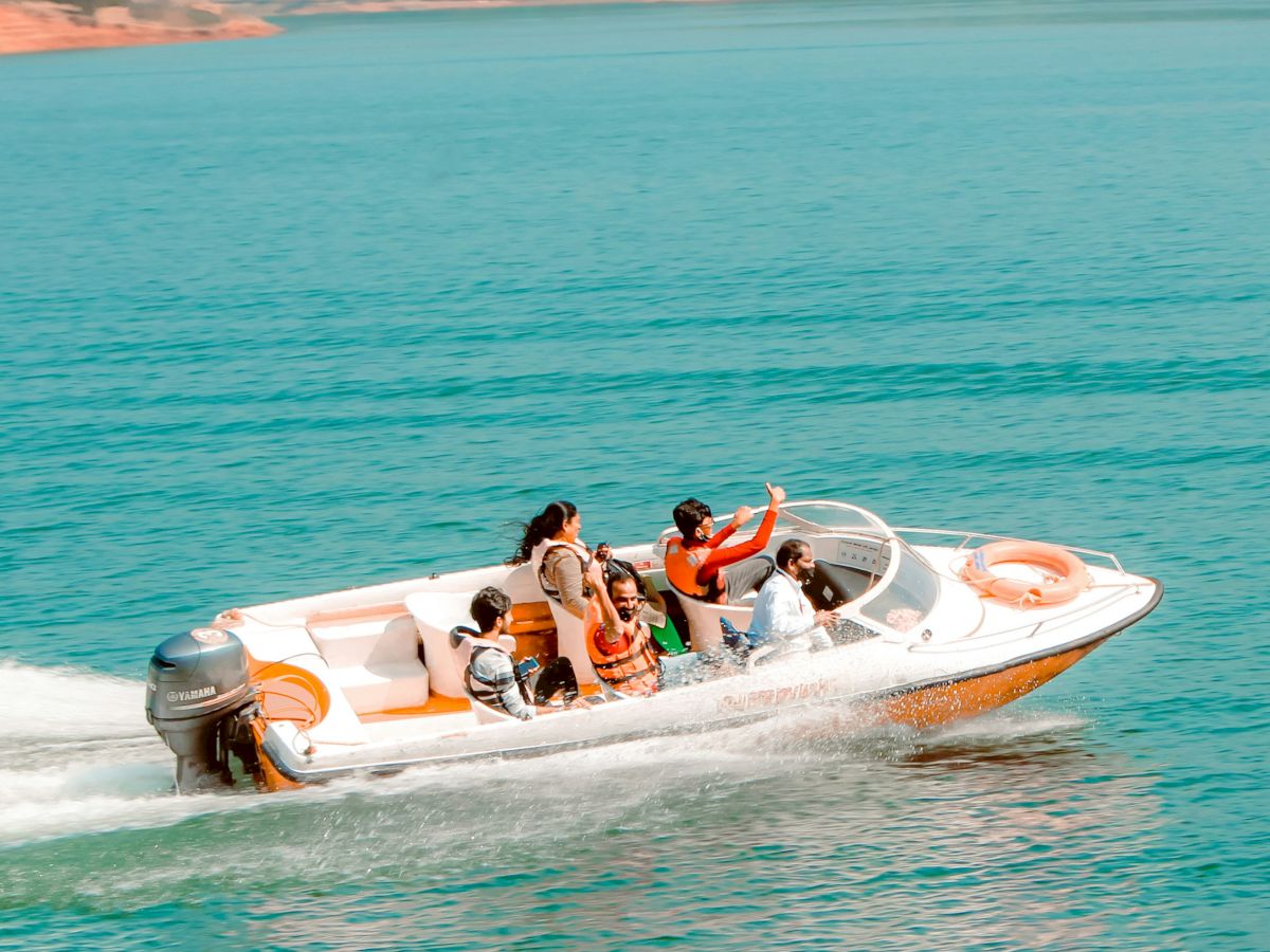 A speedboat with several people on board is cruising on a lake with lush greenery in the background, creating a lively scene.