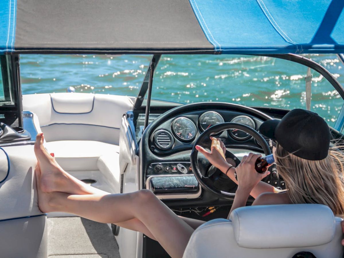 A person is lounging in a boat, steering with their feet on the dashboard while enjoying a drink under a canopy.