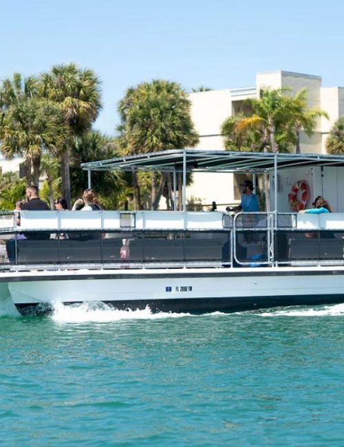 A passenger boat with people cruising on turquoise water, with palm trees and white resort buildings in the background.