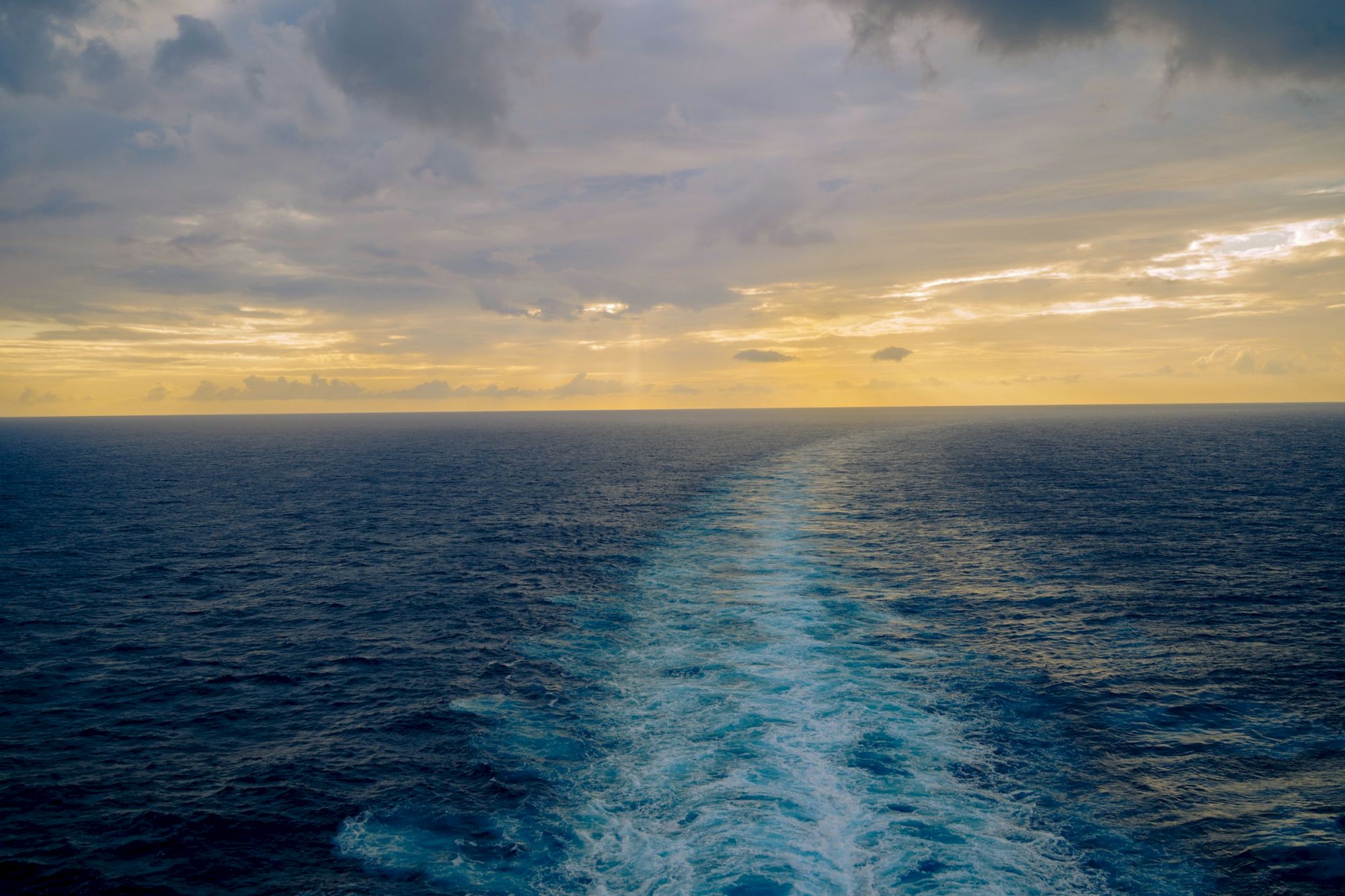 A serene ocean scene with a wake behind a boat under a cloudy sky at sunset.