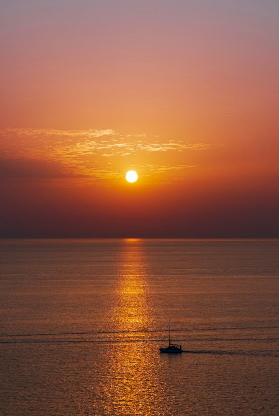 A serene sunset over a calm sea with a sailboat on the horizon and a golden reflection on the water.