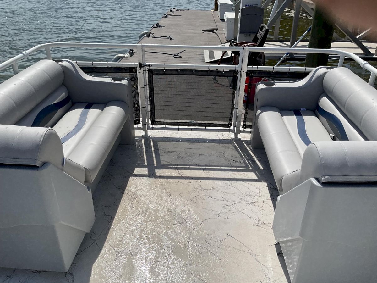 The view shows the seating and deck area of a pontoon boat on a lake, with an open gate leading to the water.