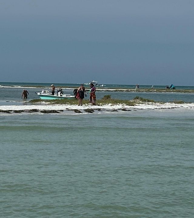 A small boat and people sit in the shallow surf on a windy beach under a gray sky.