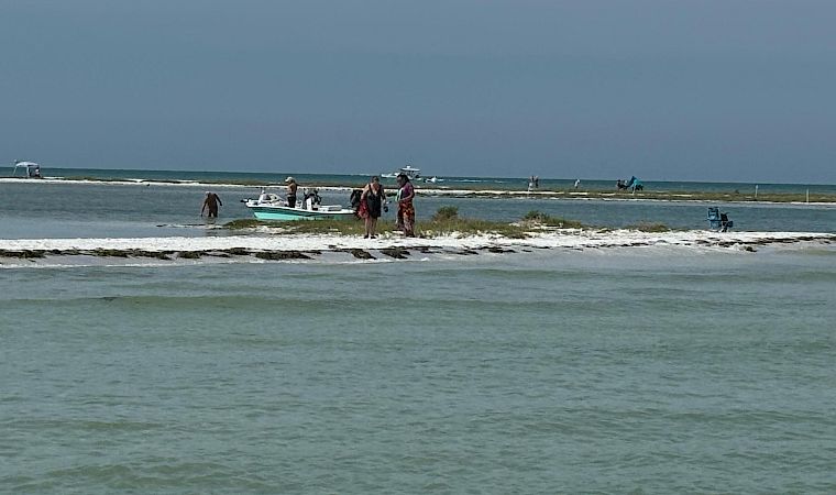A small boat and people sit in the shallow surf on a windy beach under a gray sky.