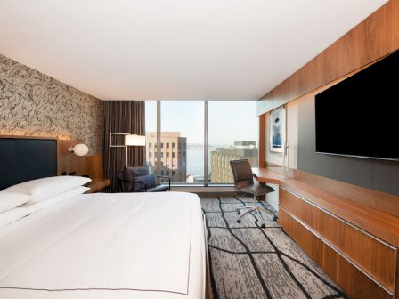 A modern hotel room with a large bed, wall-mounted TV, desk, window with city view, and stylish decor completes the setting.
