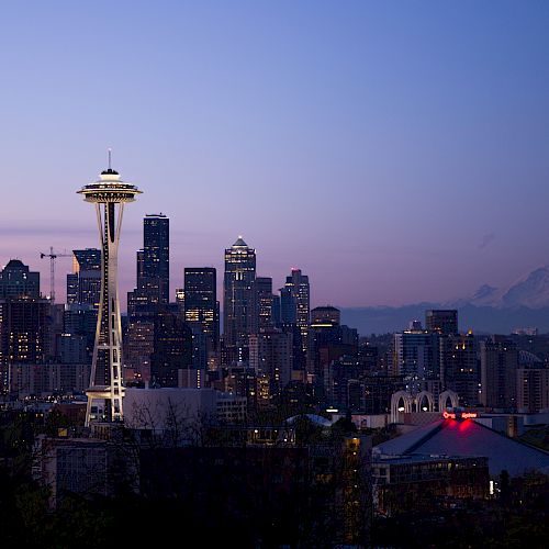Seattle skyline at dusk with the Space Needle prominently in view and Mount Rainier in the distance under a fading, colorful sky.